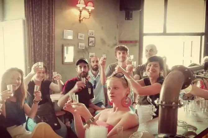Group of diverse people smiling and raising small glasses, possibly for a tasting, at a bar counter. Rustic interior with ...