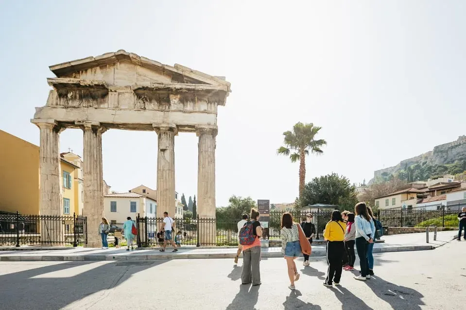 Ancient Gate of Athena Archegetis at the Roman Agora in Athens, with tourists and a palm tree on a sunny day.