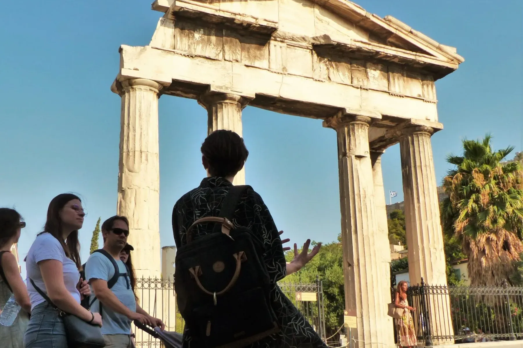 Tour group viewing the ancient Arch of Hadrian in Athens, a large stone structure with columns under a clear blue sky.