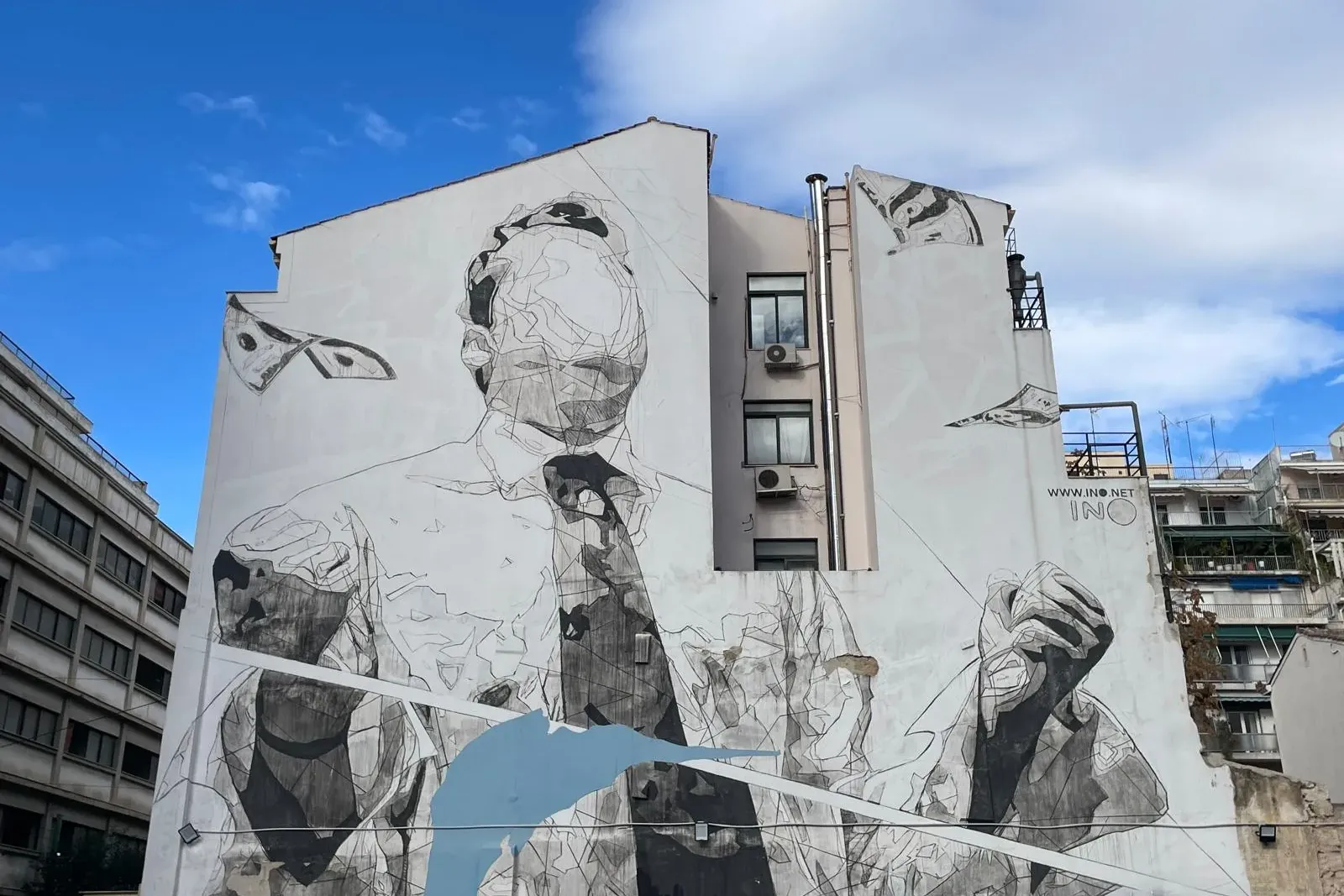 Large street art mural on a white building wall depicting a man in a shirt and tie, with flying banknotes and a blue abstr...