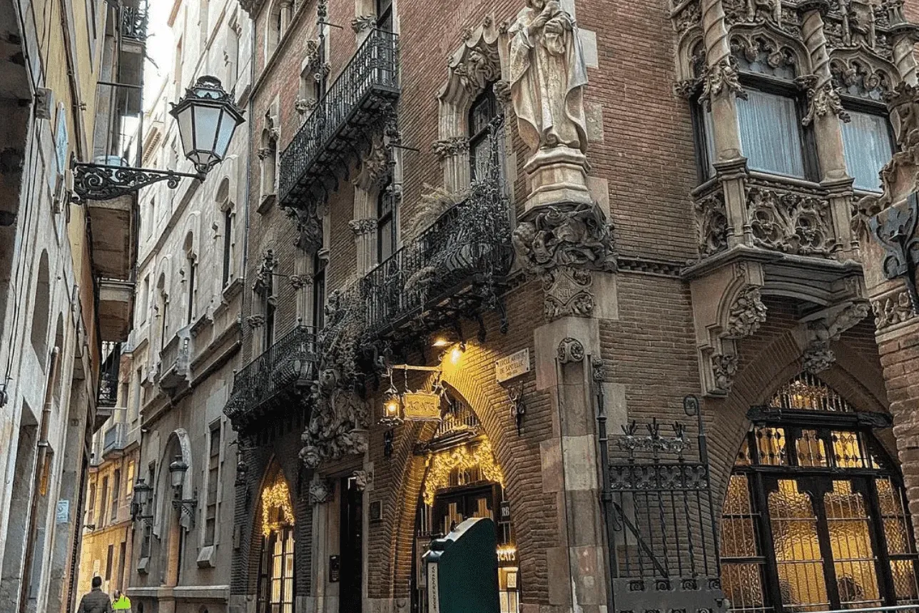 Ornate brick building with carved stone details, statue of a robed figure, decorative balconies, and lit arched windows on...