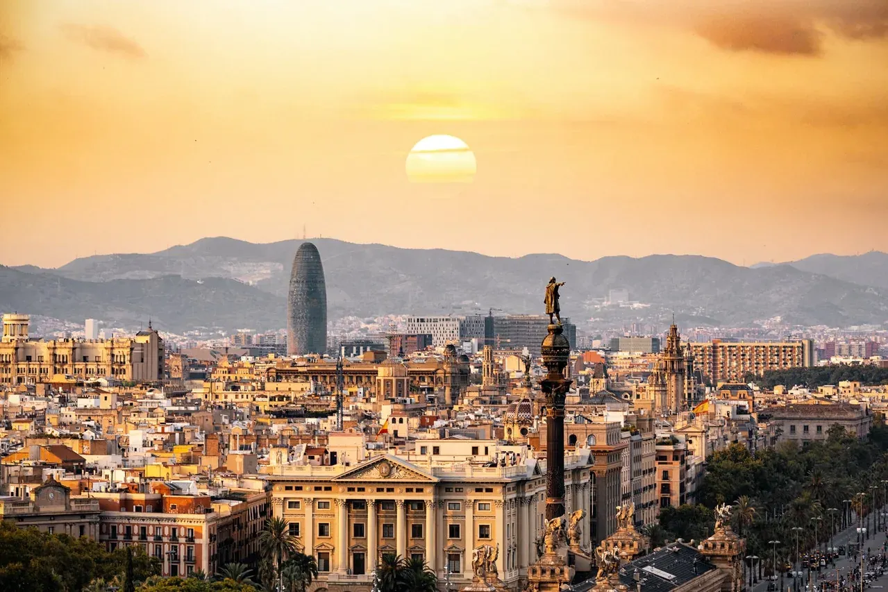 Panoramic view of Barcelona at sunset with the Columbus Monument in the foreground and Torre Glòries against a mountain ba...