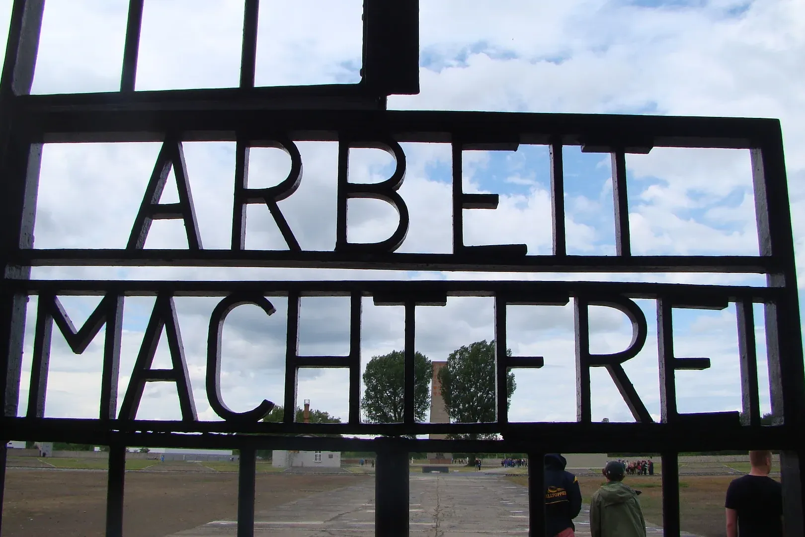 Dark metal gate with the German phrase 'ARBEIT MACHT FREI' against a cloudy sky at Sachsenhausen Memorial.