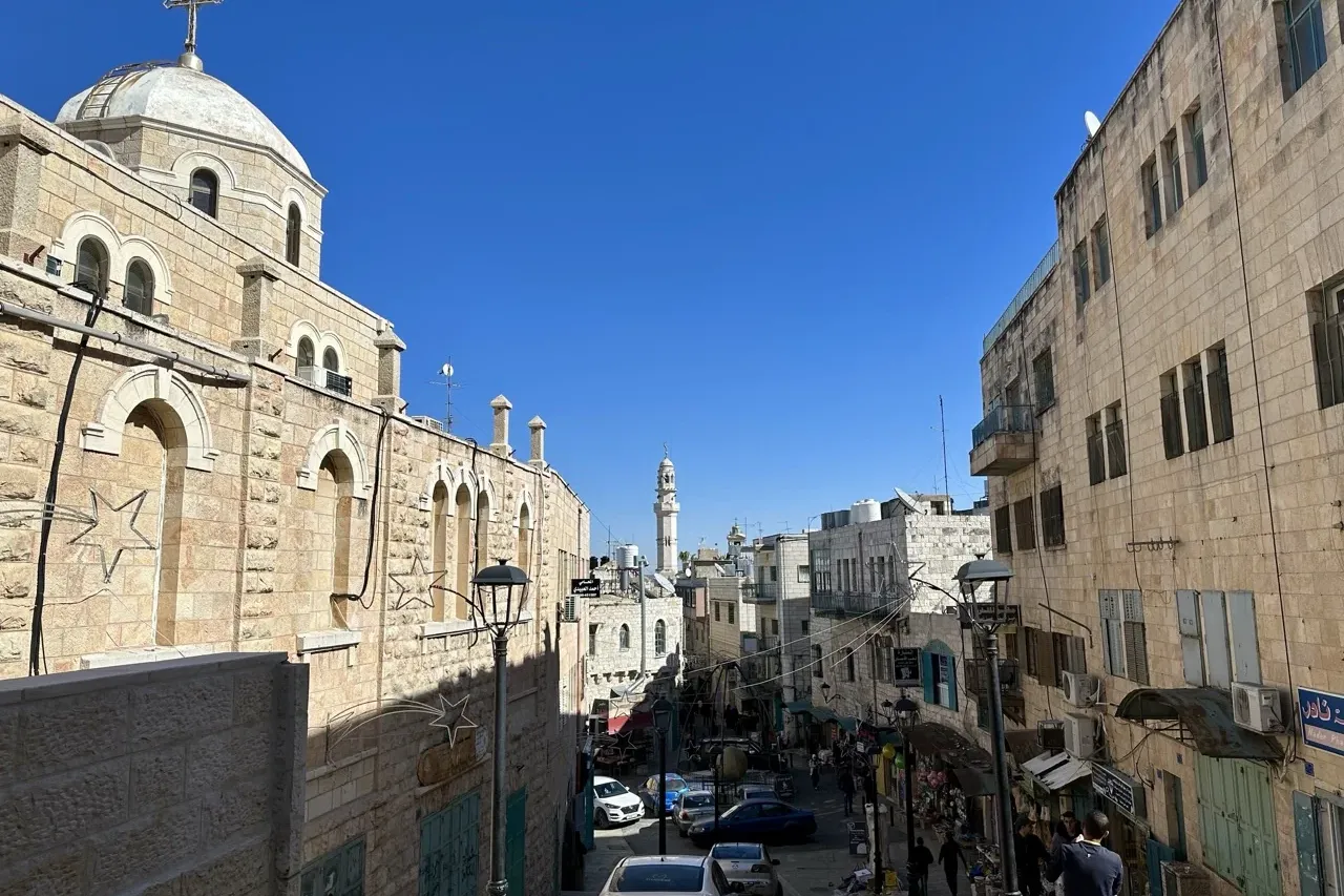 View down a stone street in Bethlehem with a large church building on the left and a distant minaret.