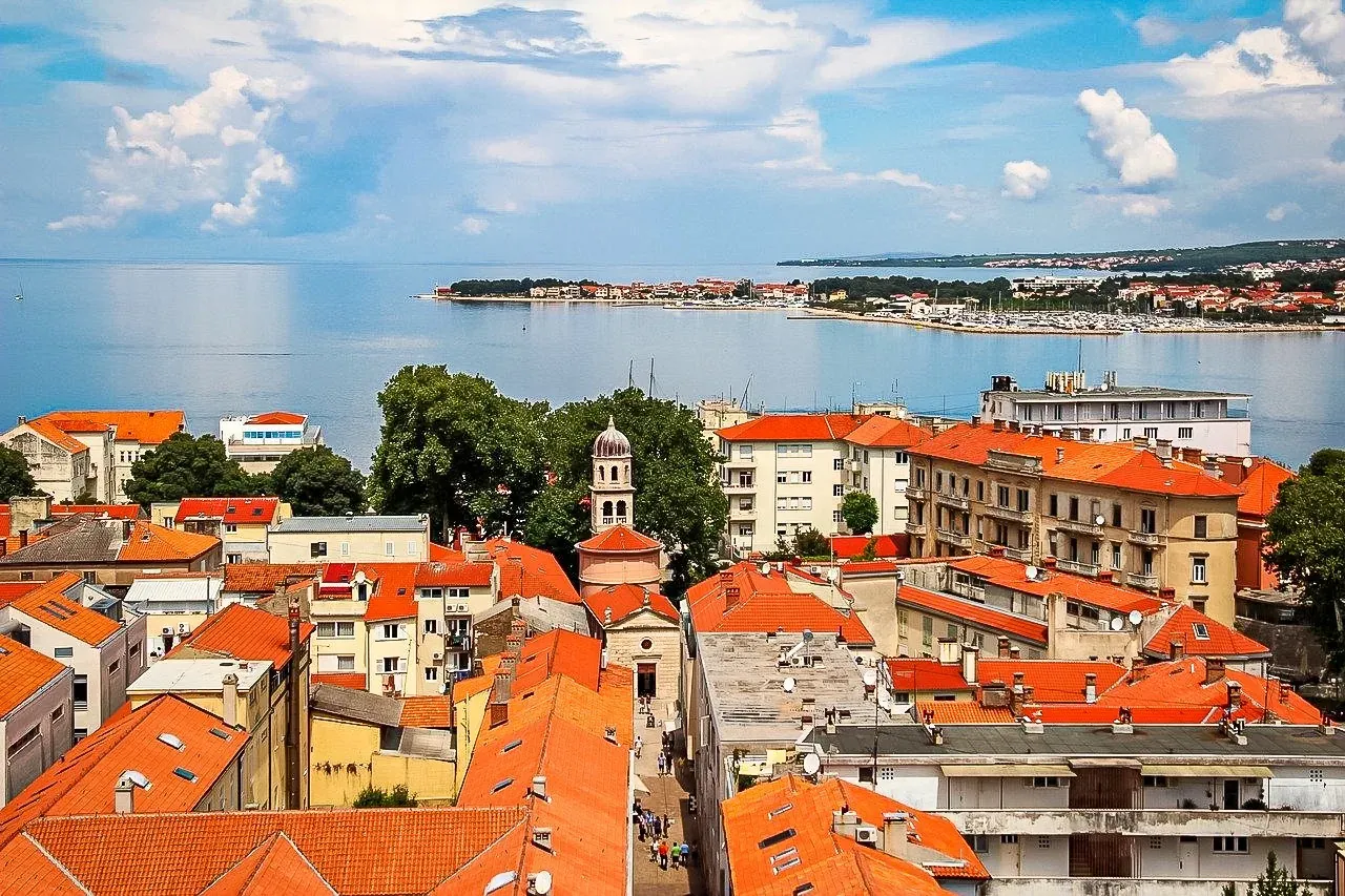 Aerial view of Zadar Old Town with orange tiled roofs, a domed bell tower, and the Adriatic Sea in the background.