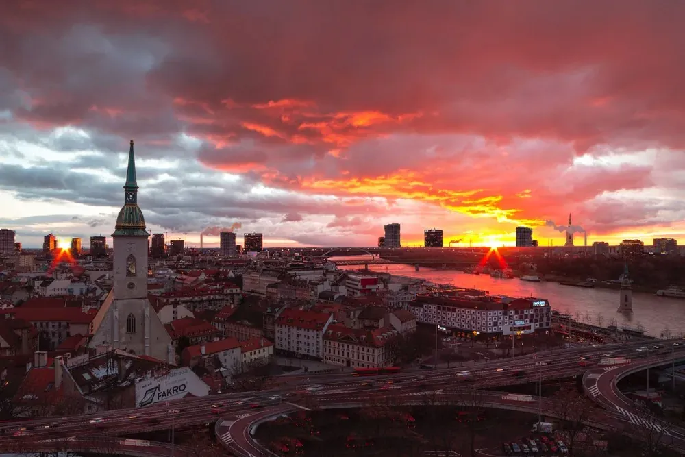 Aerial view of Bratislava at sunset with St. Martin's Cathedral, Danube river, bridges, and city skyline under a dramatic ...