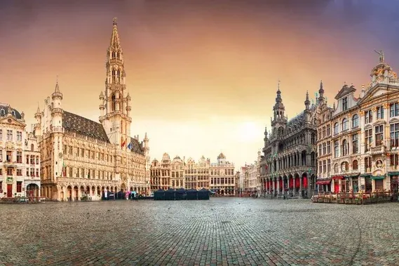 Panoramic view of Brussels Grand Place with ornate guildhalls and the Town Hall under a dramatic, colorful sky.