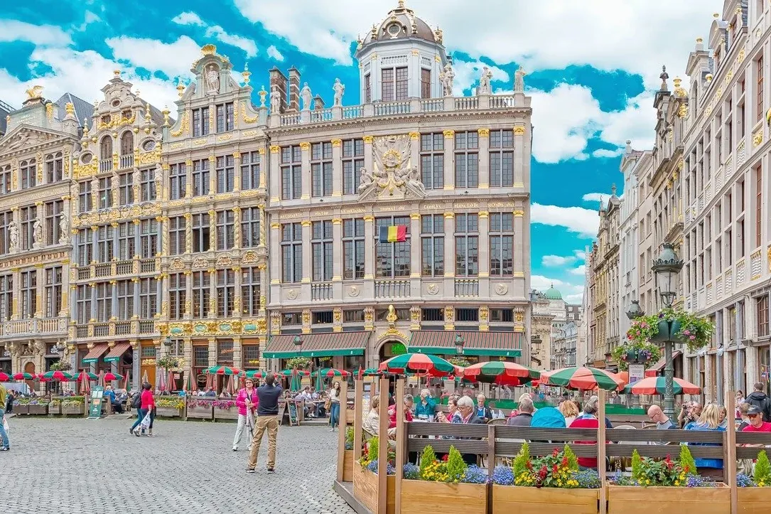 Ornate, gilded guildhalls with a Belgian flag on the Grand Place in Brussels, bustling with people and outdoor cafes under...