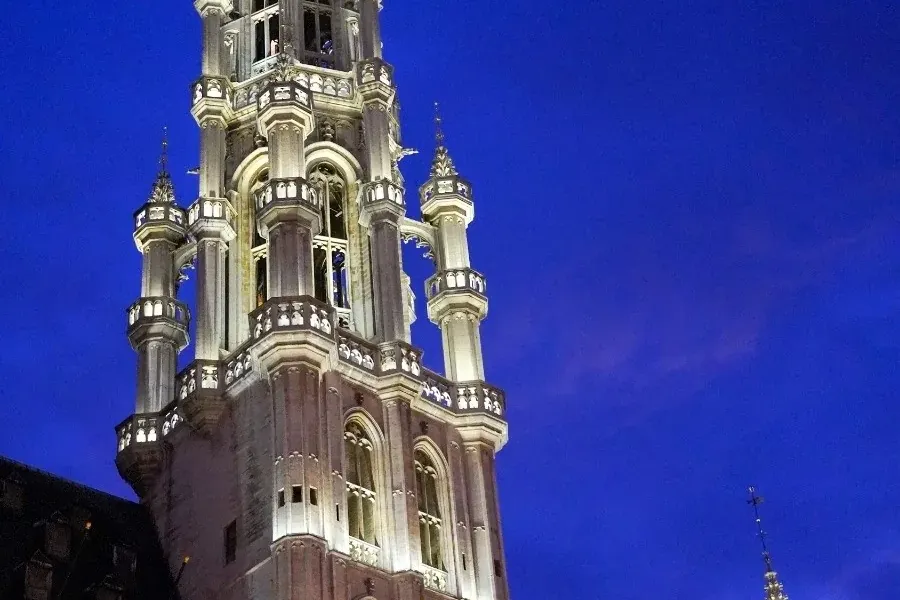Illuminated Gothic tower and facade of Brussels Town Hall under a deep blue evening sky, with Belgian and EU flags.