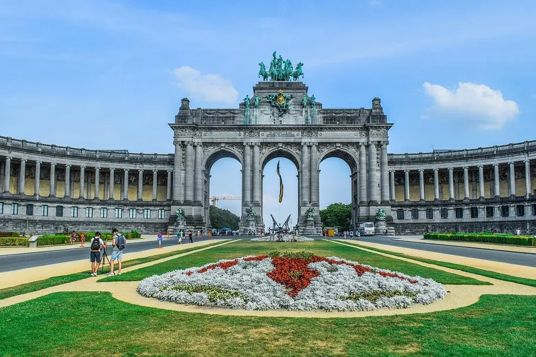 The Cinquantenaire Arch, a triple archway with a bronze quadriga, flanked by long colonnaded buildings and a park with flo...