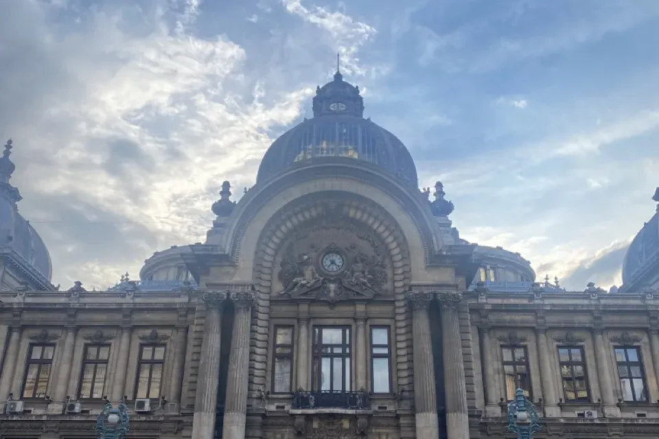 Front view of the ornate CEC Palace in Bucharest, a large building with a central dome, columns, and a clock, with a perso...