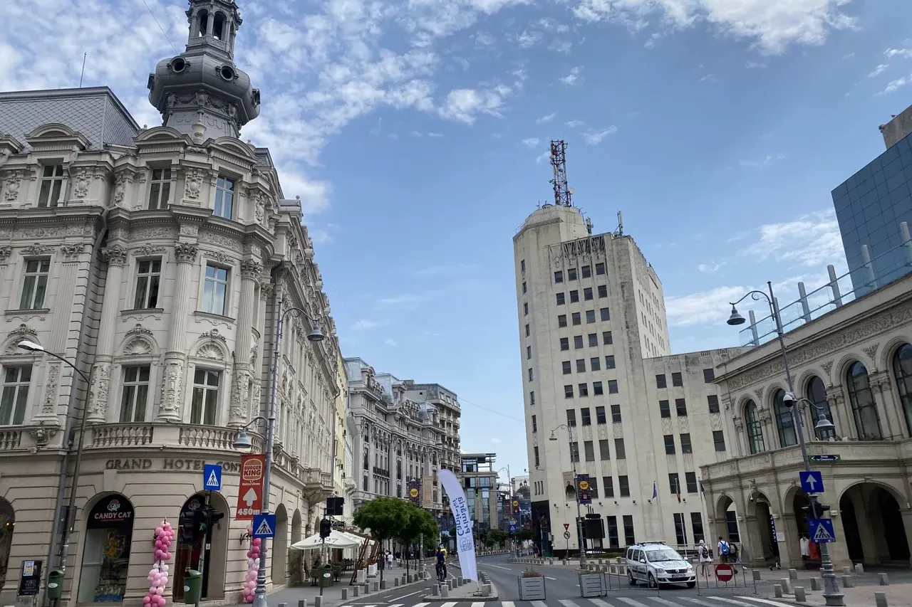 Street view in Bucharest showing the ornate Grand Hotel Continental and the tall Palatul Telefoanelor under a cloudy sky.