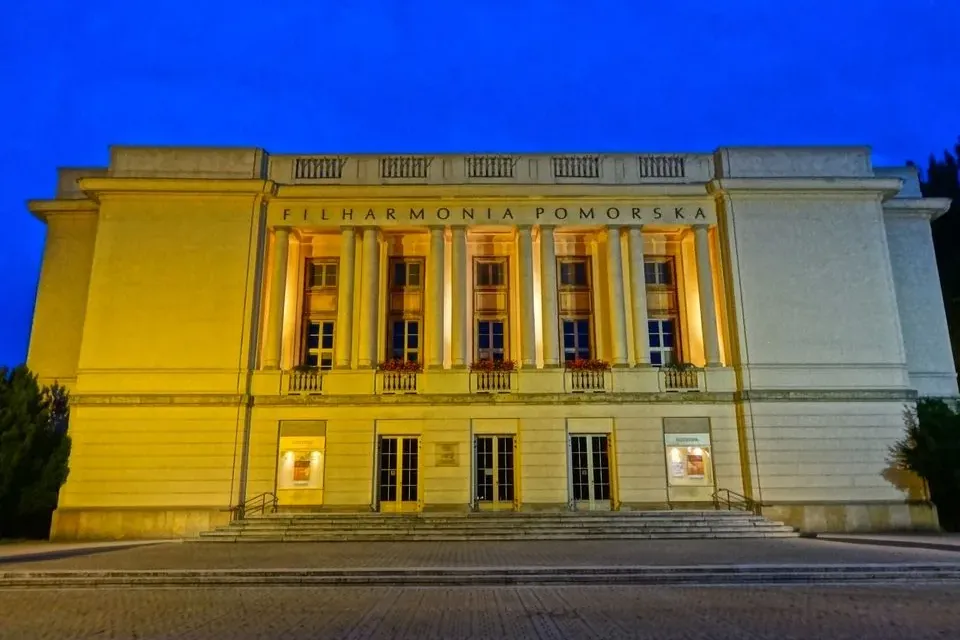 Illuminated classical building of the Pomorska Philharmonic in Bydgoszcz at night, with columns and steps under a dark blu...