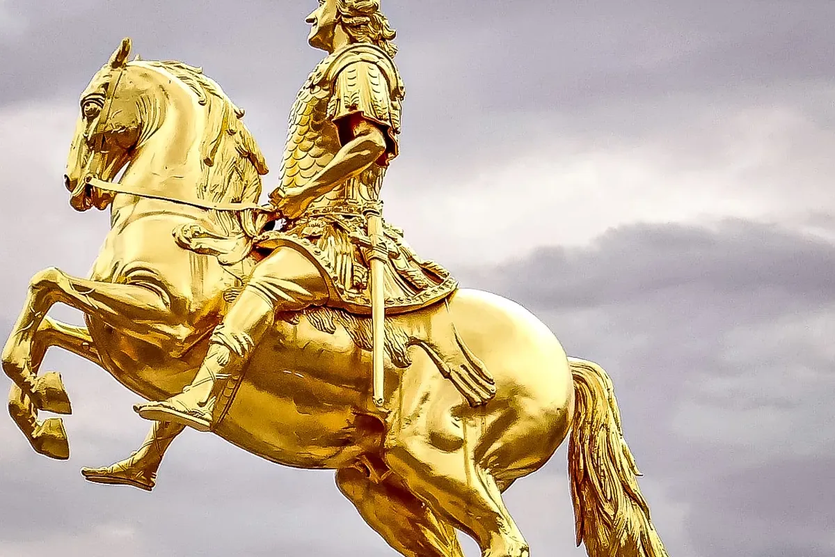 Golden equestrian statue of a man in armor on a rearing horse against a cloudy sky.