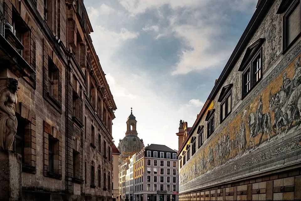 Cobblestone street in Dresden leading to Frauenkirche dome, flanked by old buildings and the Fürstenzug mural on the right.