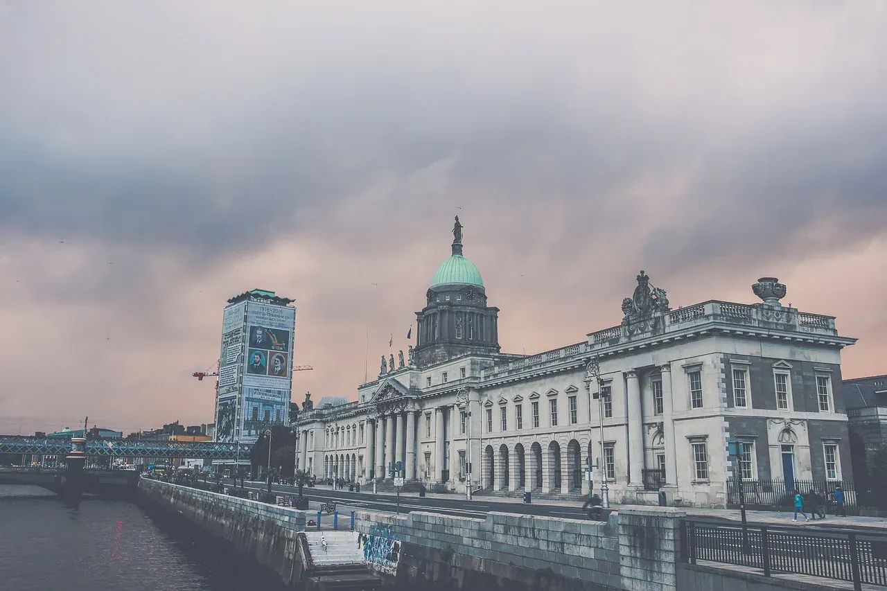 The Custom House in Dublin, a neoclassical building with a green dome, by the River Liffey under a cloudy sky.