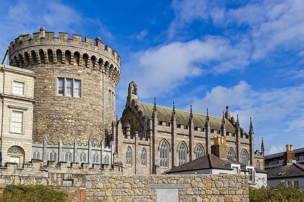 Stone round tower and ornate Gothic chapel with spires and pointed windows under a bright blue sky at Dublin Castle.