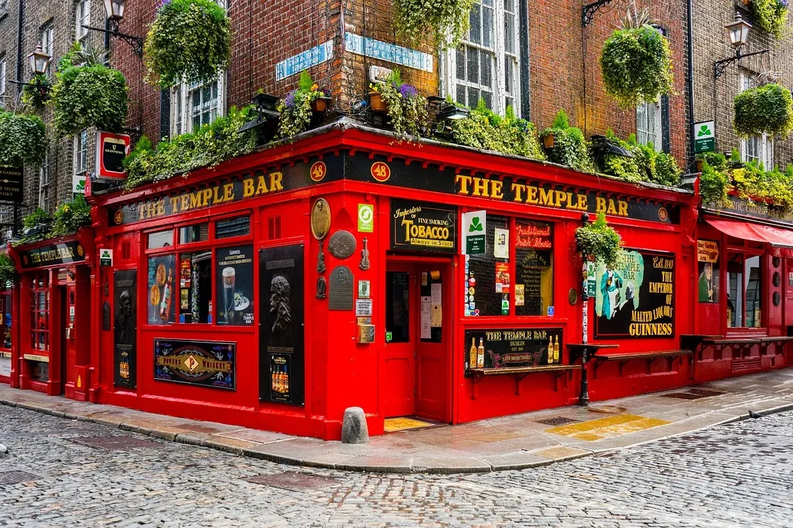 Red pub building "The Temple Bar" on a cobblestone street corner, with hanging plants and brick buildings.