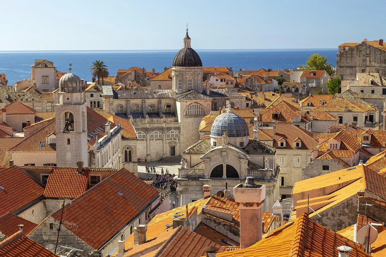 Panoramic view of Dubrovnik Old Town with terracotta roofs, historic buildings, and the Cathedral dome, leading to the blu...