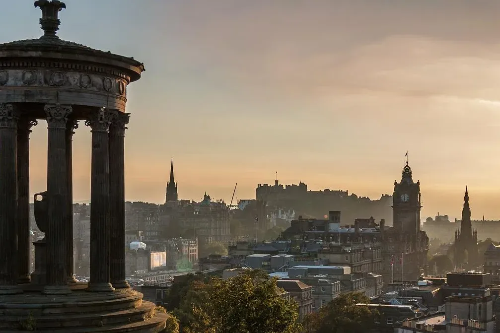 The Dugald Stewart Monument in Edinburgh's Calton Hill at sunrise, overlooking the city skyline with castle and monuments.