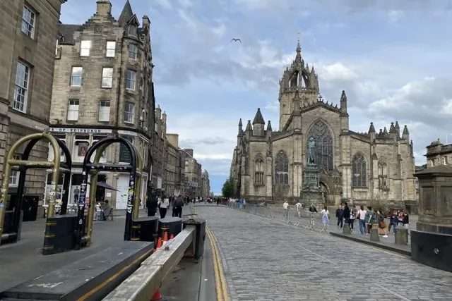 St Giles' Cathedral with its crown spire dominates a cobbled street lined with historic stone buildings and pedestrians un...