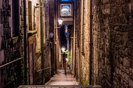 Narrow cobbled alleyway in Edinburgh at night, lined with tall stone buildings and illuminated by streetlights.