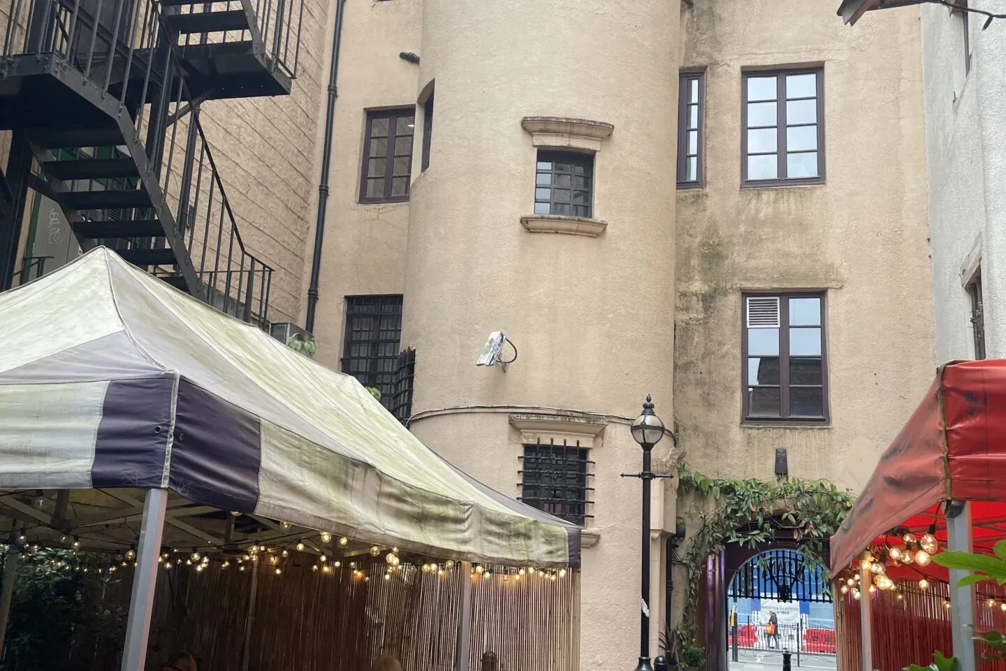 People dine at an outdoor cafe with striped awnings in a narrow cobblestone alley, surrounded by old buildings with window...