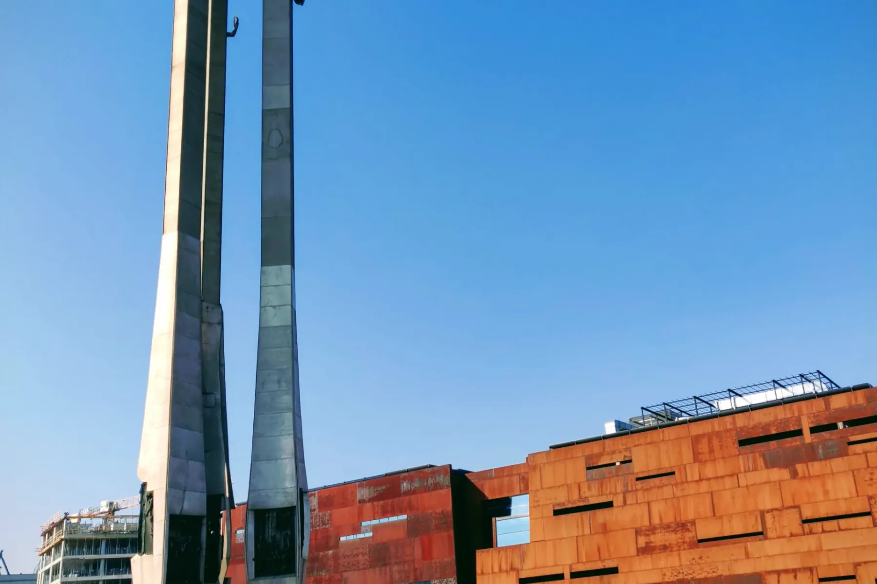 Monument to the Fallen Shipyard Workers 1970 in Gdańsk, with three tall crosses and anchors, next to a modern building wit...
