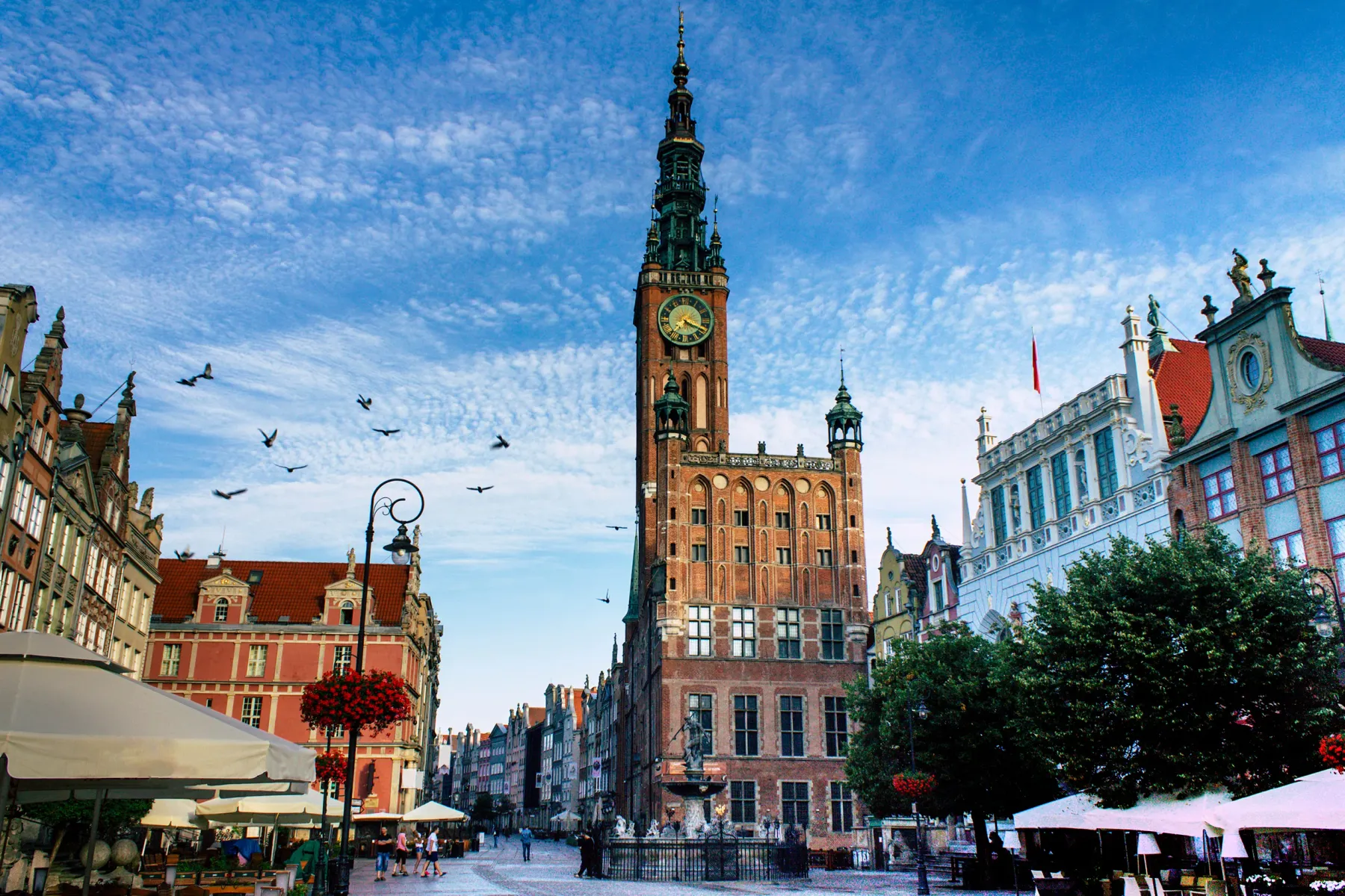 Gdansk Main Town Hall, a red brick building with a tall clock tower, standing in a lively square with people and a fountain.