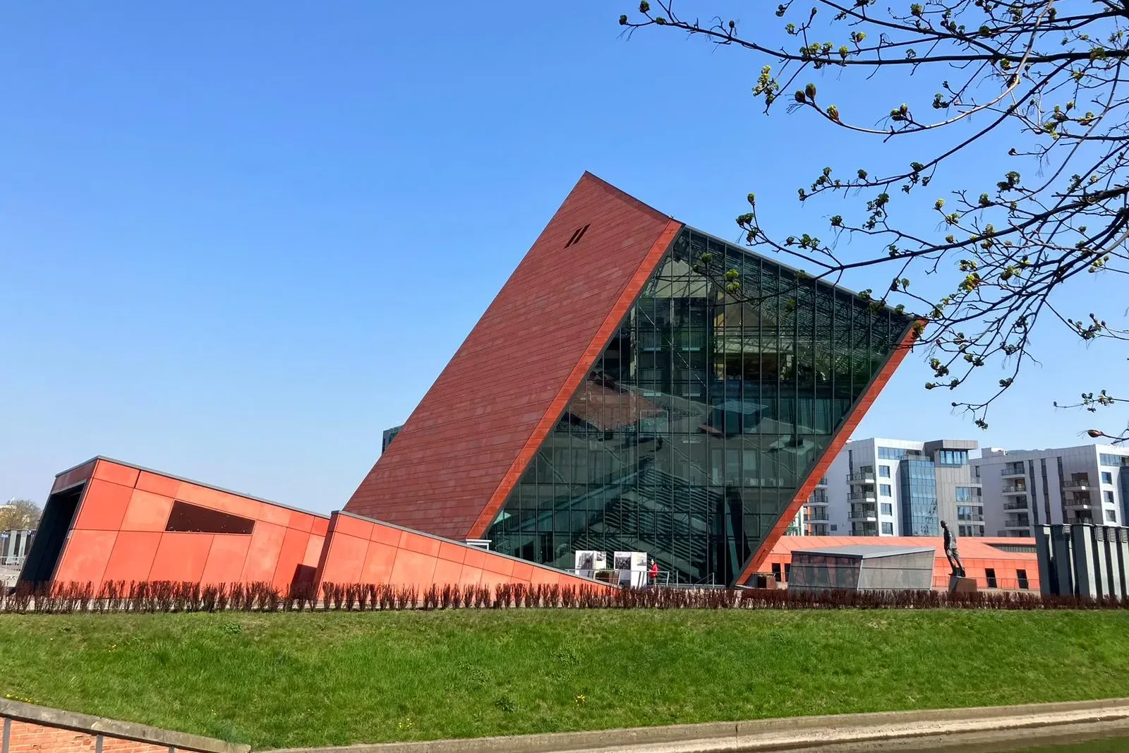 Exterior view of the Museum of the Second World War in Gdańsk, a modern building with red and glass facades, beside a canal.