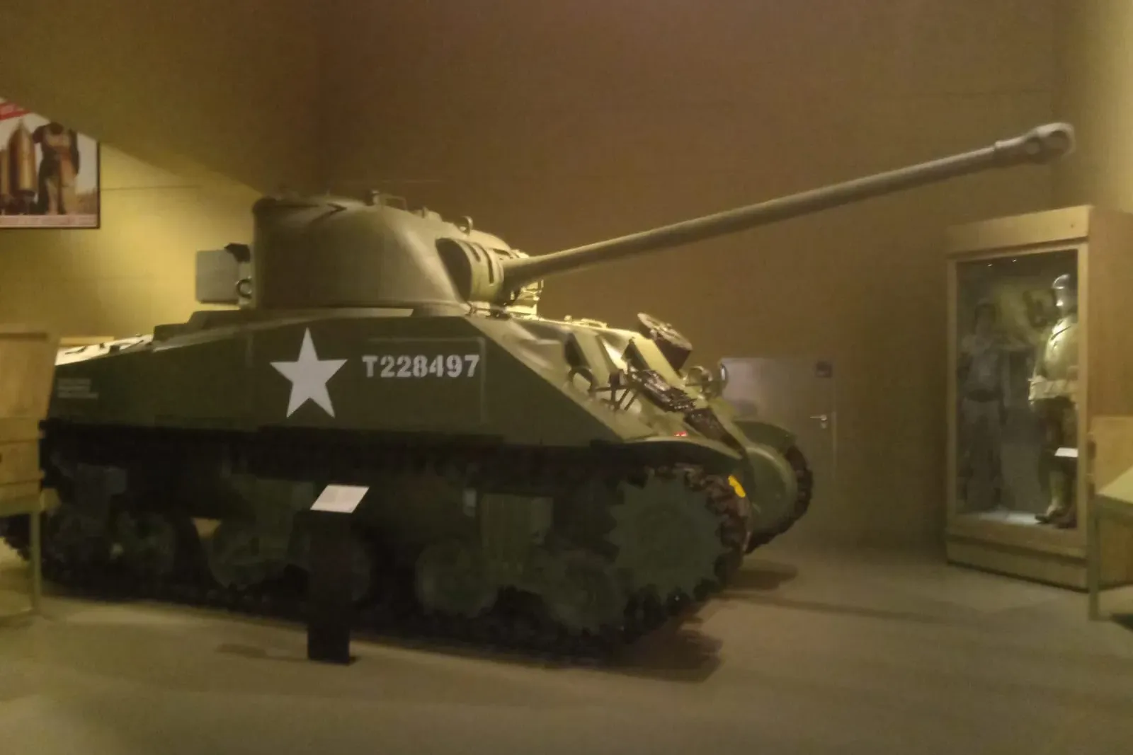 Green Sherman M4 tank with a white star and T228497 on its side, displayed in a dimly lit museum hall.