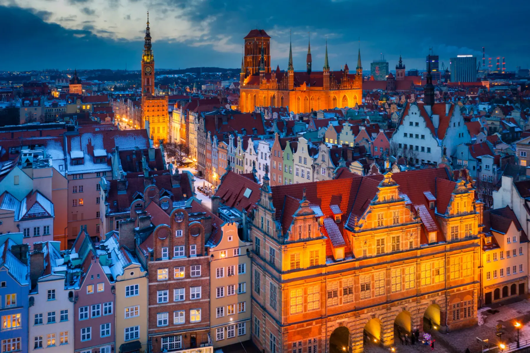 Elevated view of Gdansk Old Town at dusk. Illuminated historic buildings, snow-dusted roofs, Main Town Hall, and St. Mary'...