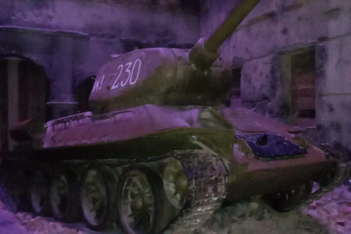 A T-34 tank with '230' painted on its turret, sitting on rubble in a dimly lit, ruined building display.