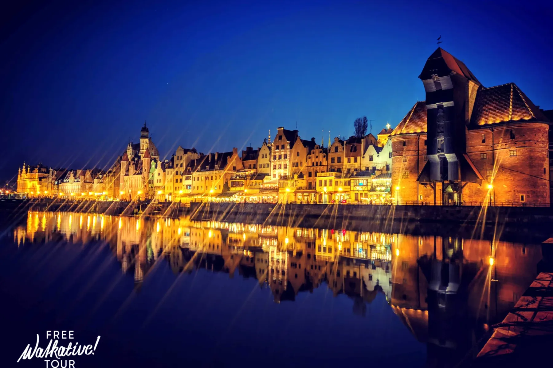 Illuminated historic buildings along a river at night, with their reflections visible in the dark water. The Gdansk Crane ...