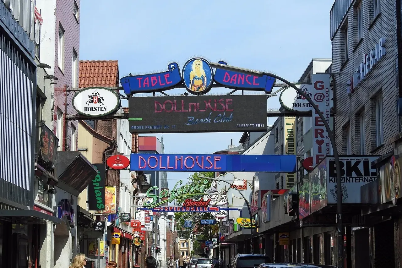 Street in Hamburg's entertainment district with many businesses, neon signs, and people walking on the sidewalk.