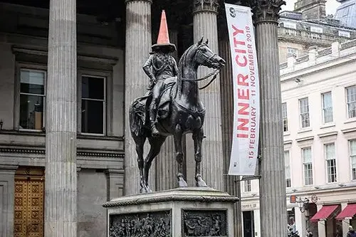 Equestrian statue of the Duke of Wellington in Glasgow city center, wearing an orange traffic cone on its head, in front o...
