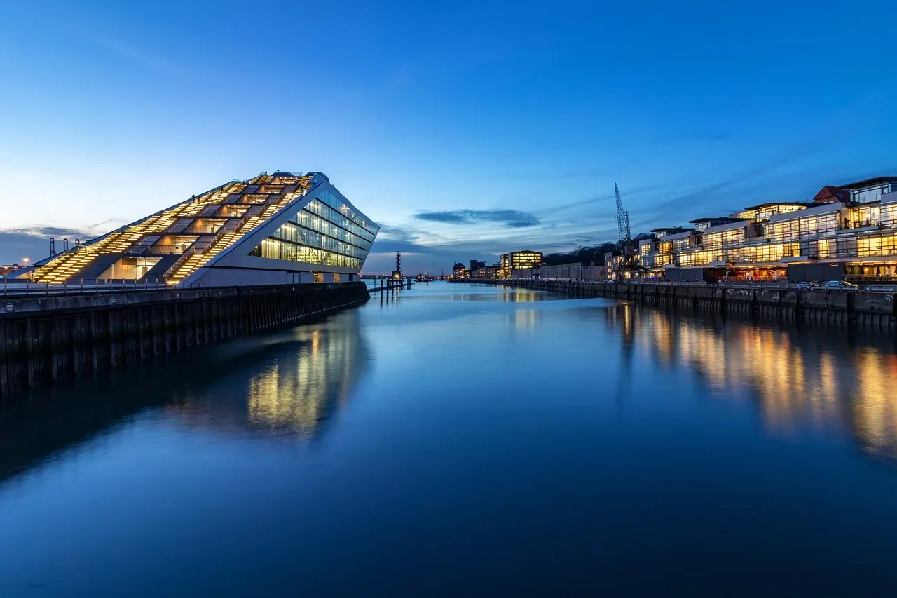 The modern Elbphilharmonie concert hall and waterfront buildings lit up at dusk, reflected in the calm waters of Hamburg's...