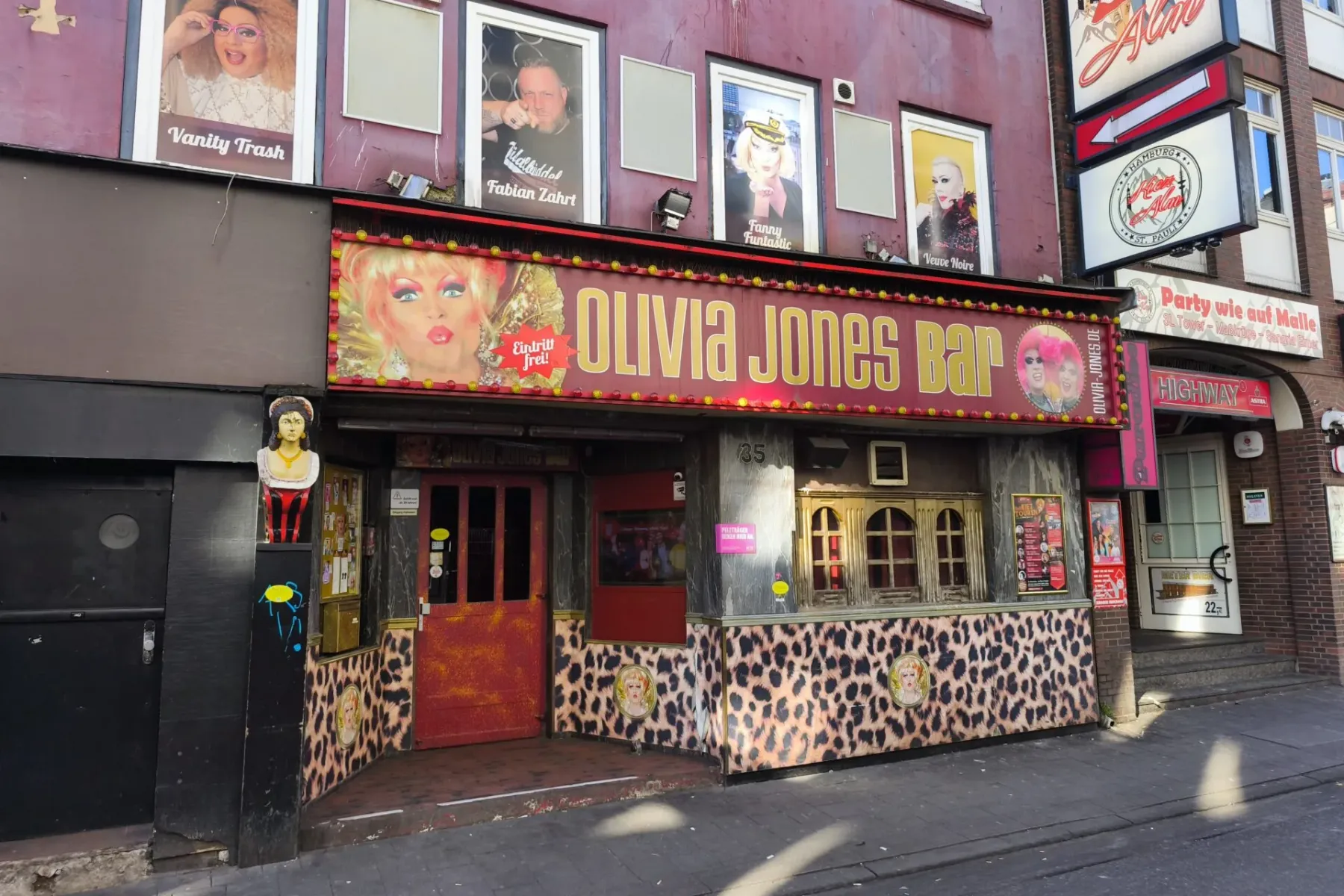 Exterior of Olivia Jones Bar in Hamburg, featuring a vibrant leopard print facade, large signage with drag queen images, a...