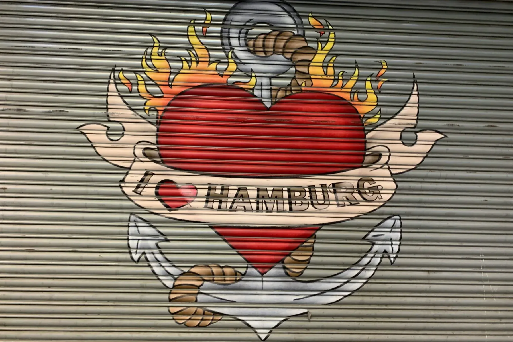 Mural on a corrugated metal roll-up door showing a red heart, an anchor, flames, and a banner with "I ♥ HAMBURG".