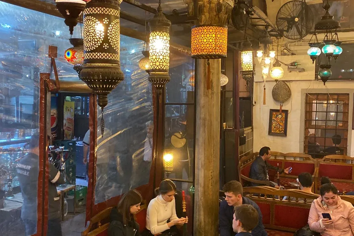 People relaxing in a traditional Istanbul tea house with ornate mosaic and metal filigree hanging lamps.