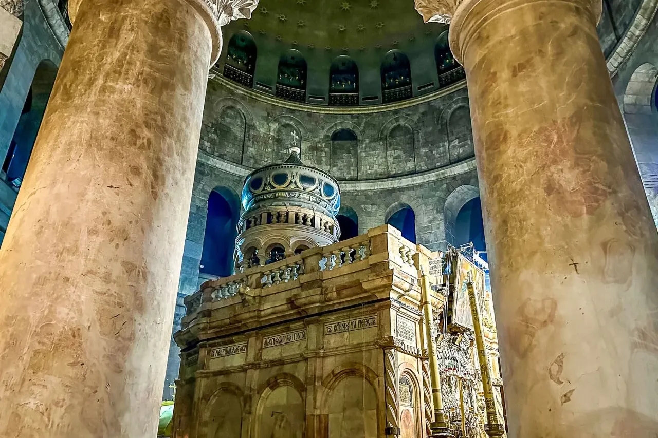 The Edicule of the Church of the Holy Sepulchre in Jerusalem, framed by two large ornate marble columns, under a vaulted d...