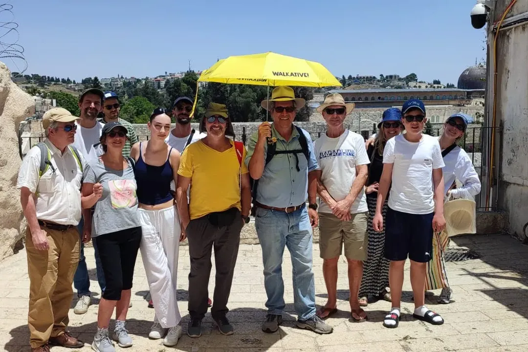 A group of tourists with a Walkative guide holding a yellow umbrella on a sunny day in Jerusalem, with the Dome of the Roc...