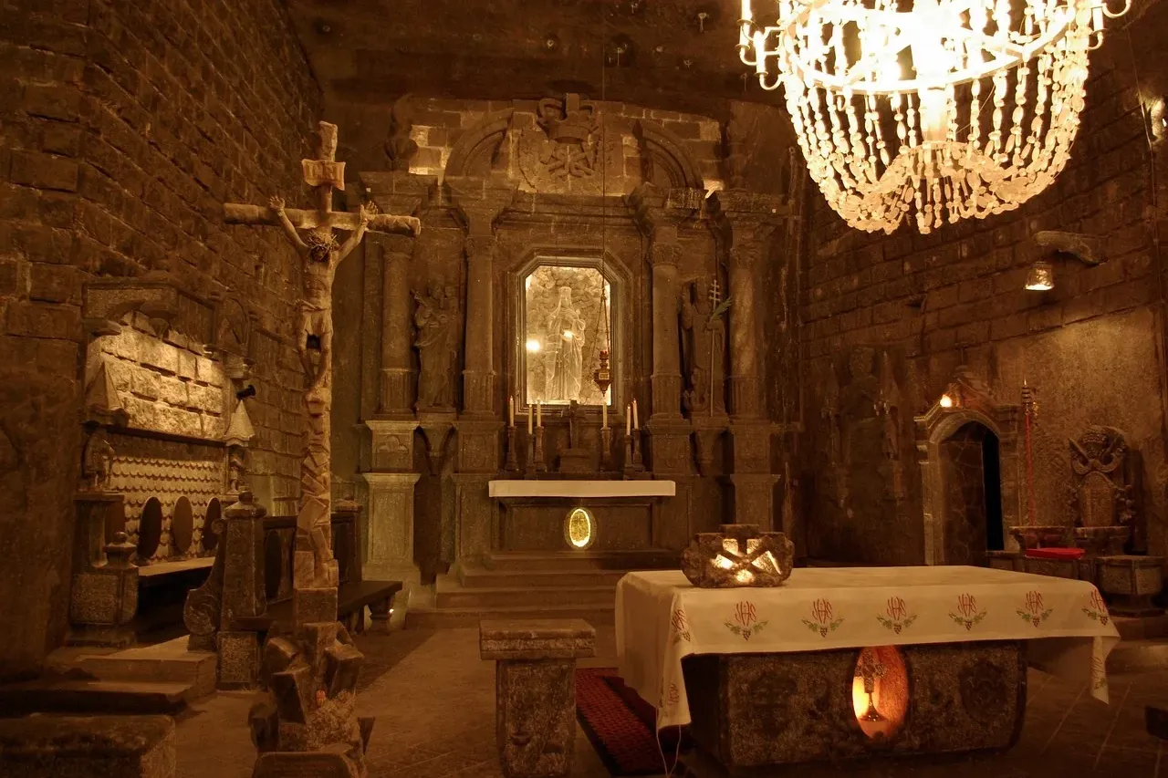 Interior of St. Kinga's Chapel in Wieliczka Salt Mine, with salt chandelier, altar, crucifix, and carved figures.
