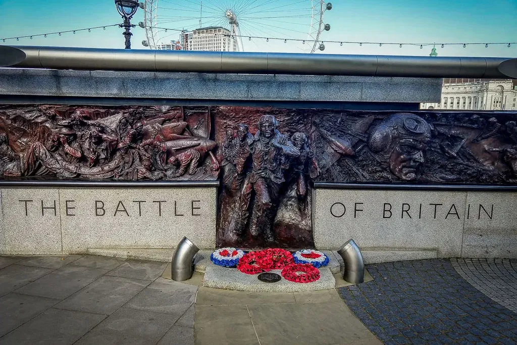 Bronze memorial for the Battle of Britain with detailed relief sculptures, wreaths, and the London Eye in the background.