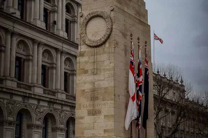 Stone Cenotaph war memorial in London with a carved wreath and "THE GLORIOUS DEAD" inscription. British flags fly under a ...
