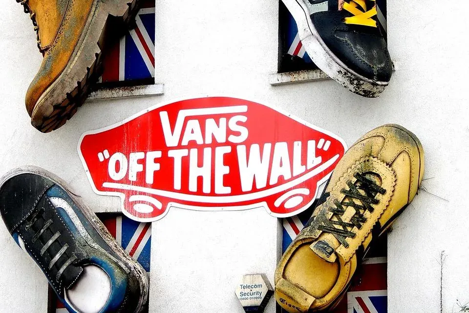 Giant decorative shoes and a red 'Vans Off The Wall' sign on a white building wall. Union Jack flags are visible in windows.