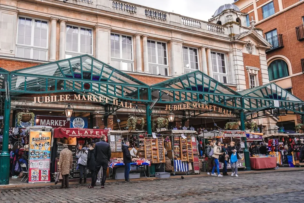 Jubilee Market Hall in London with a green glass canopy over market stalls and people browsing on a cobbled street.