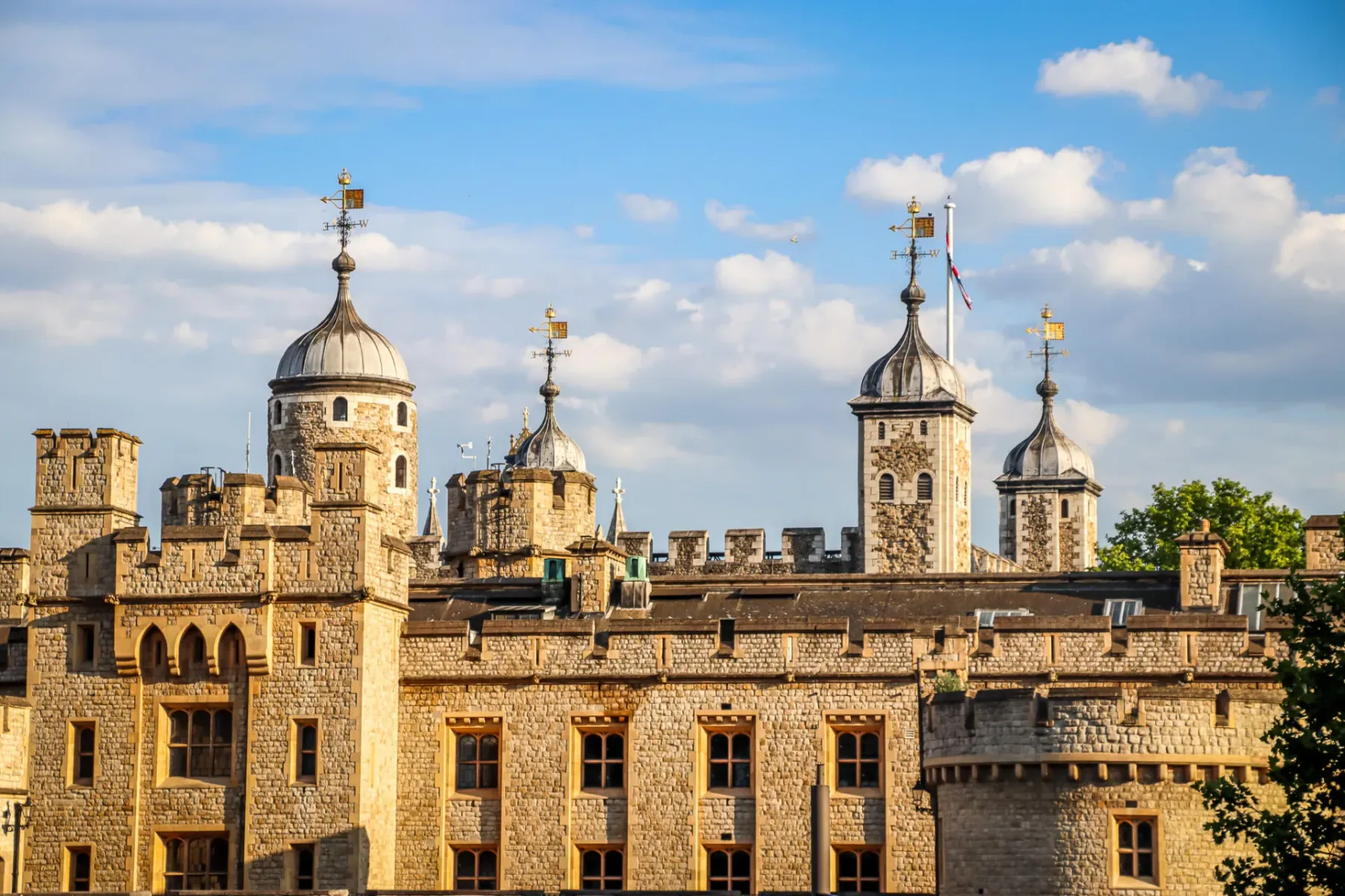 Close-up of the Tower of London's stone walls and multiple grey-domed turrets under a blue sky with white clouds.