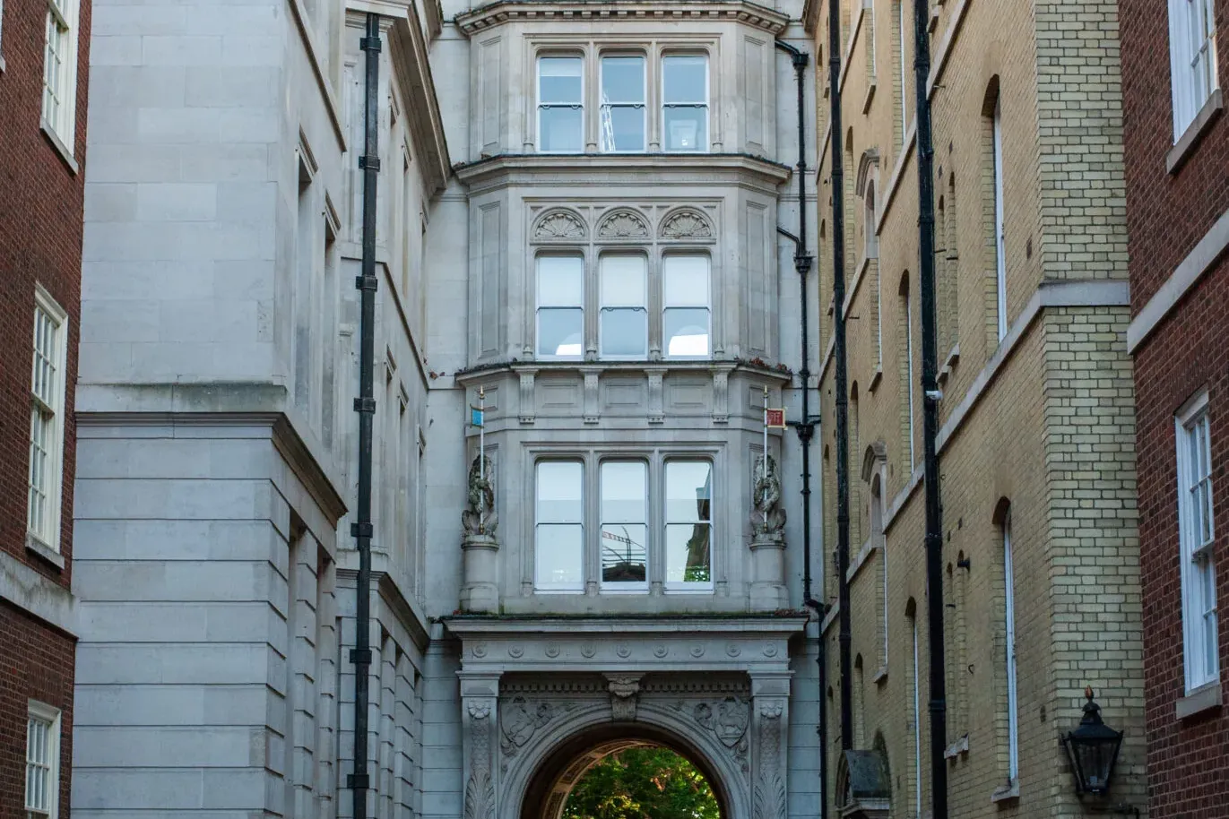 A narrow paved alleyway in London, flanked by historic stone and brick buildings. A person with a yellow Walkative umbrell...