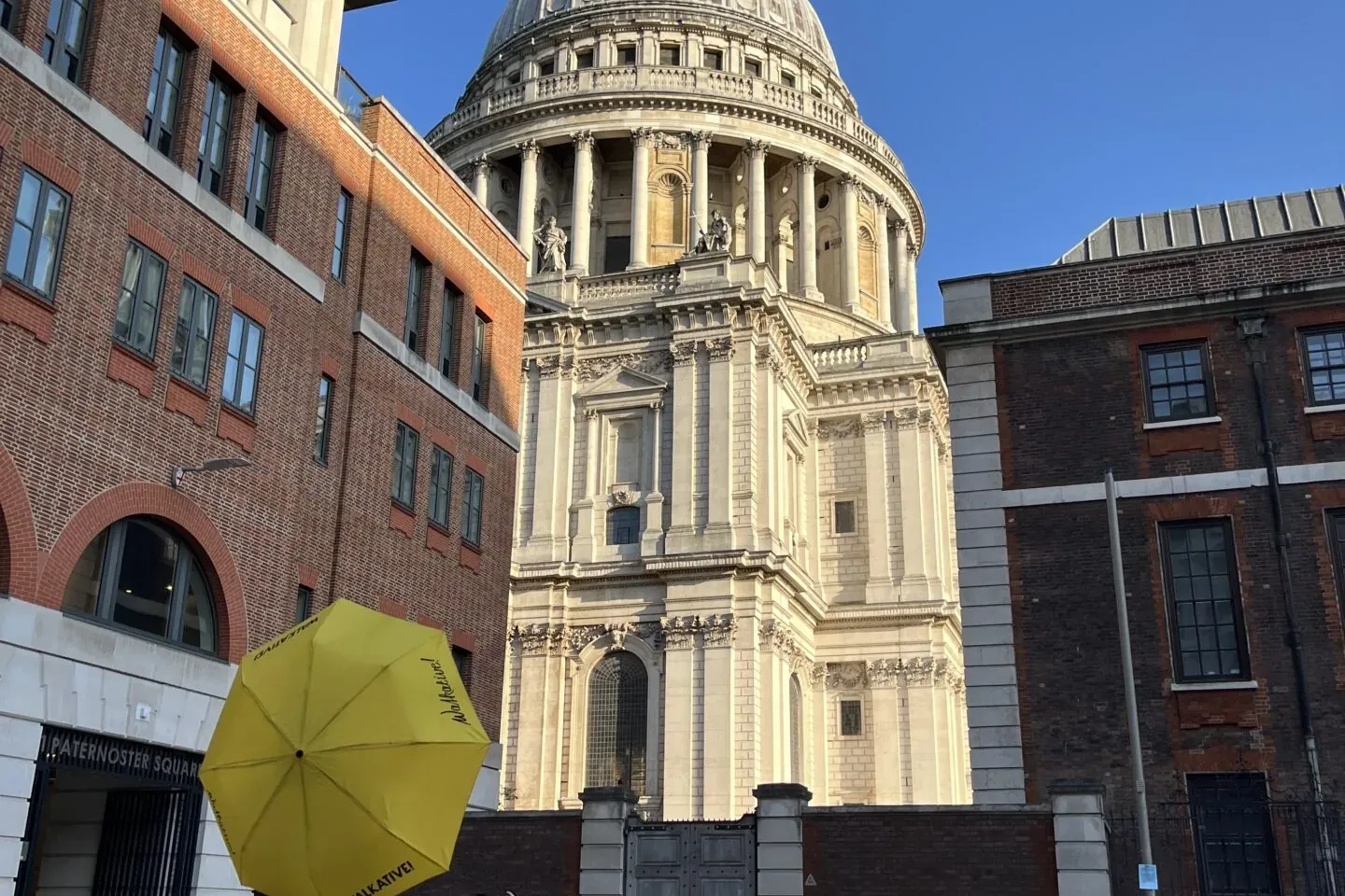 A person holding a yellow Walkative umbrella stands facing St Paul's Cathedral in London. Paternoster Square is in the for...
